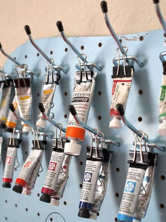 Hooks of the pegboard holding painting tubes.