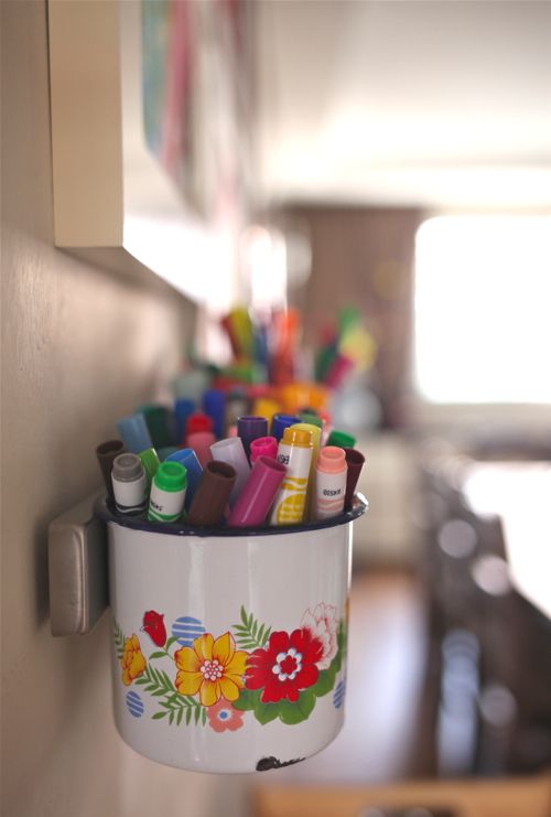 Magnetic strip holding metal container carrying art supplies like markers and paint brushes.