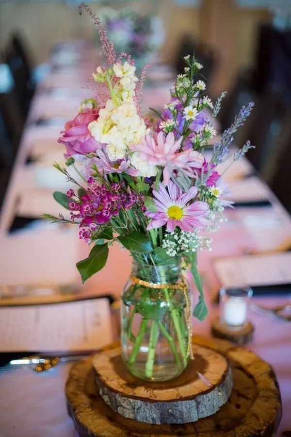 Pink and purple blooms in display on a driftwood tray inside a tiny mason jar.