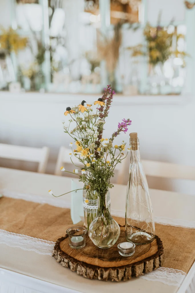 Rustic elegance for a wildflower centrepiece with a fairy light glass bottle and tiny votive on a wooden coaster.