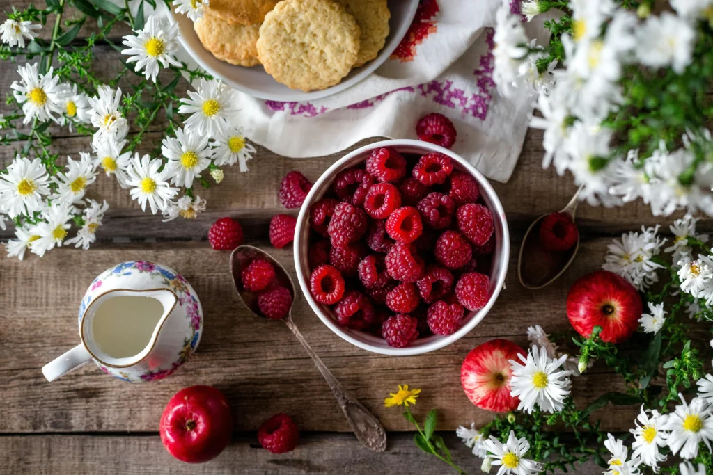 A bowl of berries with chamomile flowers on a rustic table with a china teapot.